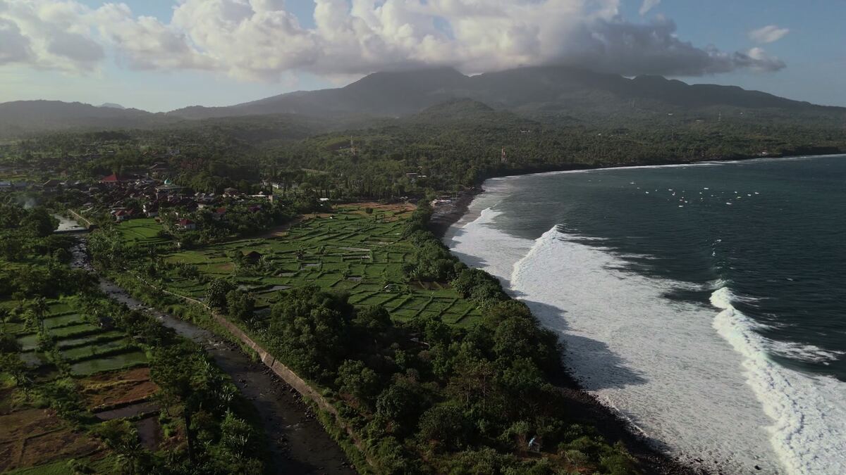 Sawah, desa, sungai dan pantai Karangasem di Bali Timur dengan pegunungan di belakangnya, difoto dari drone